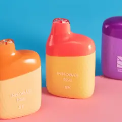 Trois vapoteuses colorées, orange, jaune et violette, sur fond bleu et rose. Attention à la remontée liquide dans la bouche.