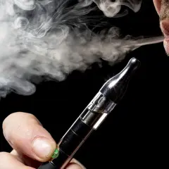 Un homme exhale une vapeur dense d'une cigarette électronique, un geste qui peut représenter un bienfait pour certains.