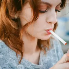 Une jeune femme aux cheveux roux allume une cigarette électronique, signe d'une possible addiction.