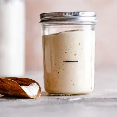 Un bocal de levain pétillant, prêt à amorcer la résistance d'une pâte à pain. Une cuillère en bois contient de la farine.