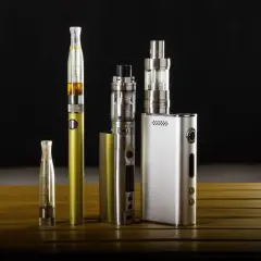 Collection de cigarettes électroniques, dont une dorée et une argentée, sur une table en bois. Ces appareils de vapotage, souvent à basse tension, offrent une alternative moderne.