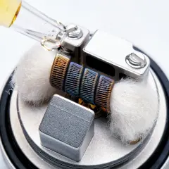 Goutte d'e-liquide sur un atomiseur prêt à l'emploi, avec ses mèches de coton et sa résistance colorée.