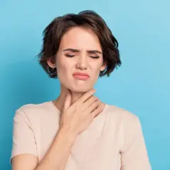 Femme avec la main sur la gorge, grimace, possible irritation due à une cigarette électronique gorge serrée.