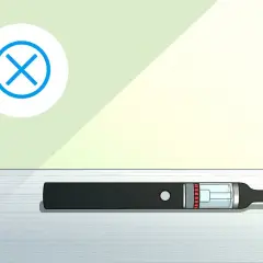 Une cigarette électronique noire est posée sur une surface. Un cercle blanc avec une croix bleue indique que le vuse clignote 3 fois, signalant un problème.