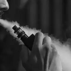 Un homme tire sur une cigarette électronique, exhalant un nuage de vapeur. Il ressent fatigue et vertiges.
