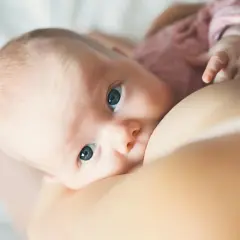 Un bébé aux grands yeux bleus tète le sein de sa mère. L'allaitement est un moment précieux, loin des préoccupations comme la cigarette électronique.