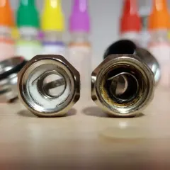 Deux résistances de cigarette électronique sur une table en bois. L'une est neuve, l'autre montre les signes d'une résistance crâmée après avoir vapoté.