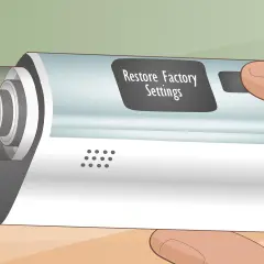 Main d'une personne tenant un appareil électronique avec un écran affichant "Restore Factory Settings". L'atomizer est visible sur le côté gauche.