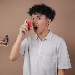 Un jeune homme utilise son inhalateur pour l'asthme, tandis qu'une cigarette électronique et des cigarettes sont présentées de chaque côté, soulignant les dangers.