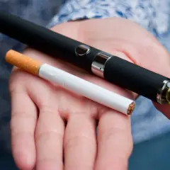 Témoignage arrêt tabac : une cigarette électronique et une cigarette classique sont tenues dans une main, symbolisant le passage à une alternative.