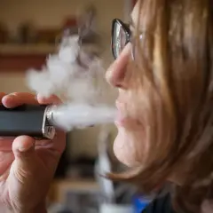 Une femme tire sur sa cigarette électronique, mais elle ne tire plus. La vapeur s'échappe.