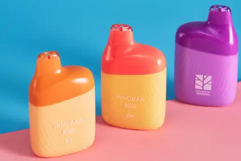Trois vapoteuses colorées, orange, jaune et violette, sur fond bleu et rose. Attention à la remontée liquide dans la bouche.