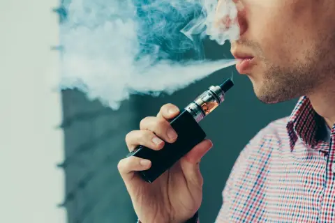 Un homme exhale de la vapeur d'une cigarette électronique. Avis sur ce produit, un choix pour certains.