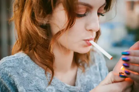 Une jeune femme aux cheveux roux allume une cigarette électronique, signe d'une possible addiction.