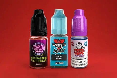 Trois flacons de e-liquide Vampire Vape, dont un Heisenberg, sur fond rouge.