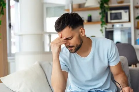 Homme fatigué se tenant la tête, peut-être à cause d'une cigarette électronique et d'un mal de tête.