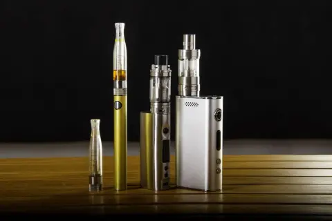 Collection de cigarettes électroniques, dont une dorée et une argentée, sur une table en bois. Ces appareils de vapotage, souvent à basse tension, offrent une alternative moderne.
