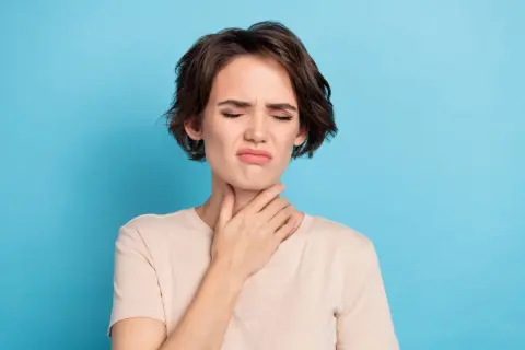 Femme avec la main sur la gorge, grimace, possible irritation due à une cigarette électronique gorge serrée.