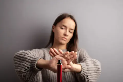 Une jeune femme refuse le montage cigarette électronique, les mains croisées en signe d'arrêt.