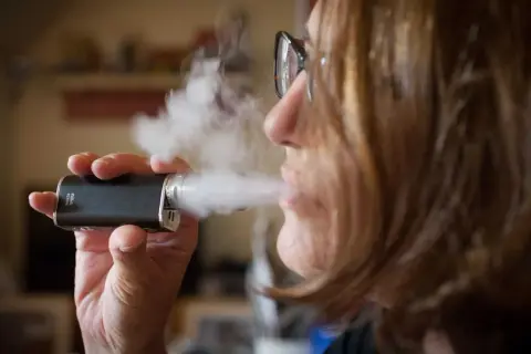 Une femme tire sur sa cigarette électronique, mais elle ne tire plus. La vapeur s'échappe.