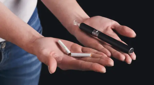 Deux mains présentent un choix : une cigarette électronique et une cigarette cassée. Un symbole pour arrêter de fumer.