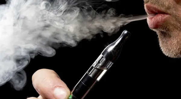 Un homme exhale une vapeur dense d'une cigarette électronique, un geste qui peut représenter un bienfait pour certains.