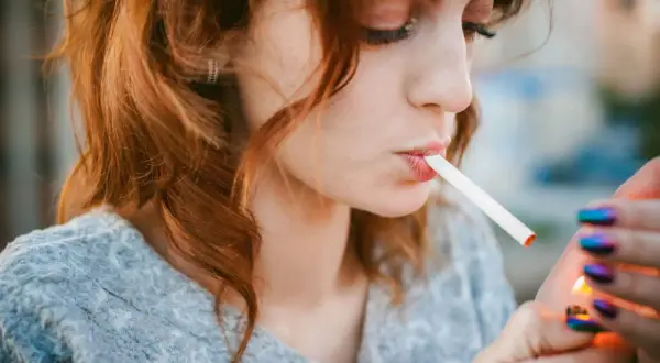 Une jeune femme aux cheveux roux allume une cigarette électronique, signe d'une possible addiction.