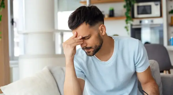 Homme fatigué se tenant la tête, peut-être à cause d'une cigarette électronique et d'un mal de tête.