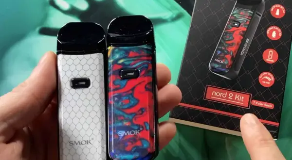 Deux vapoteuses Smok Nord 2, une blanche à motifs nid d'abeille, l'autre colorée. La boîte du kit Smok Nord 2 est visible.