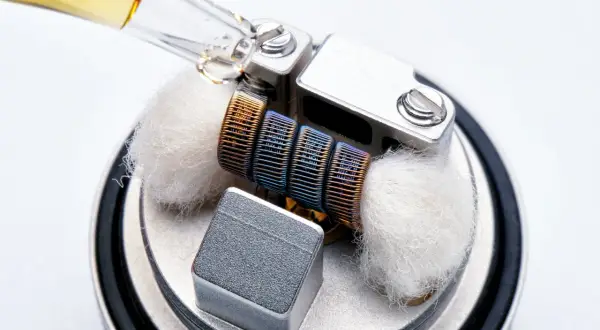 Goutte d'e-liquide sur un atomiseur prêt à l'emploi, avec ses mèches de coton et sa résistance colorée.