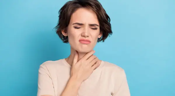 Femme avec la main sur la gorge, grimace, possible irritation due à une cigarette électronique gorge serrée.