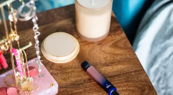 Sur la table de nuit, une cigarette blu clignote bleu. À côté, des bijoux et une bougie.