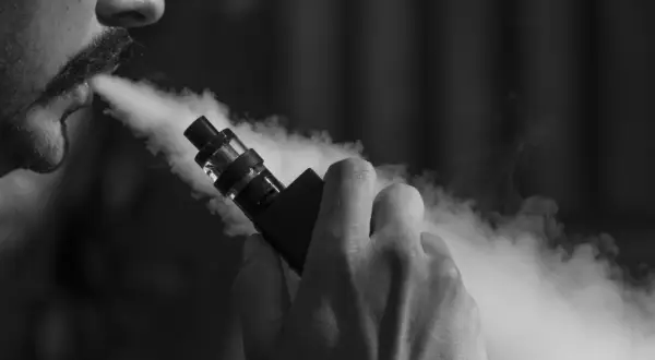 Un homme tire sur une cigarette électronique, exhalant un nuage de vapeur. Il ressent fatigue et vertiges.