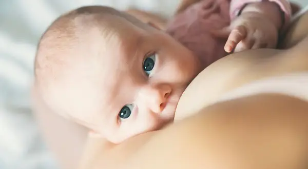 Un bébé aux grands yeux bleus tète le sein de sa mère. L'allaitement est un moment précieux, loin des préoccupations comme la cigarette électronique.