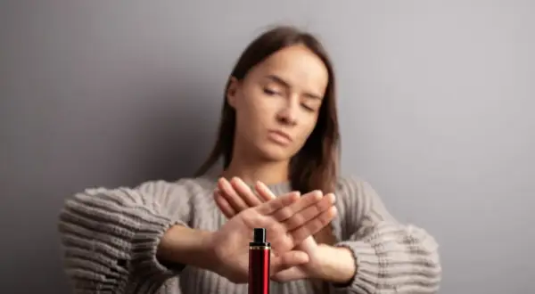 Une jeune femme refuse le montage cigarette électronique, les mains croisées en signe d'arrêt.