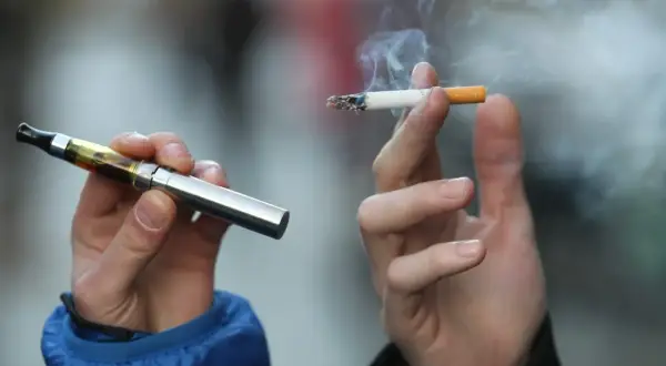 Deux mains tiennent une cigarette électronique et une cigarette allumée, symbolisant les différentes formes de consommation de nicotine et leur origine.