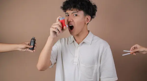 Un jeune homme utilise son inhalateur pour l'asthme, tandis qu'une cigarette électronique et des cigarettes sont présentées de chaque côté, soulignant les dangers.