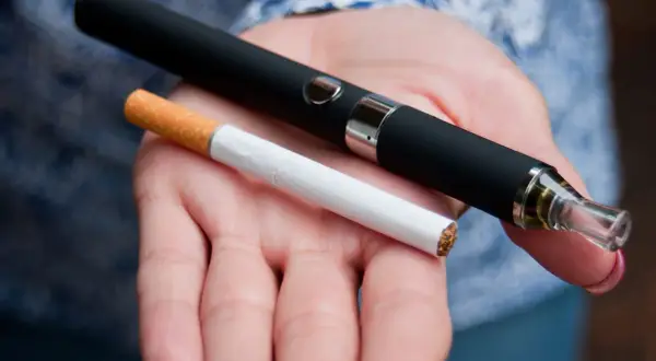 Témoignage arrêt tabac : une cigarette électronique et une cigarette classique sont tenues dans une main, symbolisant le passage à une alternative.