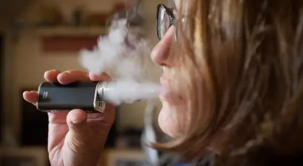 Une femme tire sur sa cigarette électronique, mais elle ne tire plus. La vapeur s'échappe.