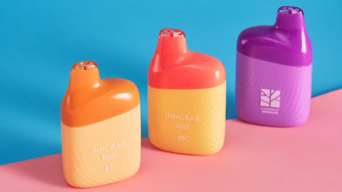 Trois vapoteuses colorées, orange, jaune et violette, sur fond bleu et rose. Attention à la remontée liquide dans la bouche.