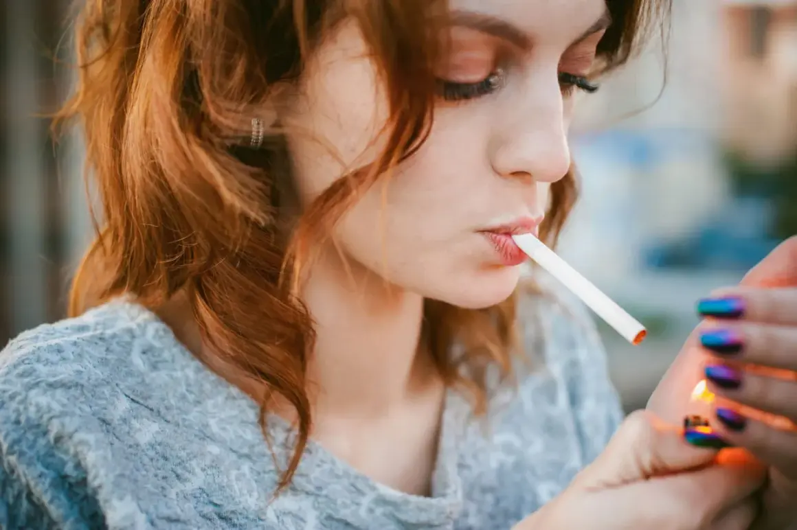 Une jeune femme aux cheveux roux allume une cigarette électronique, signe d'une possible addiction.