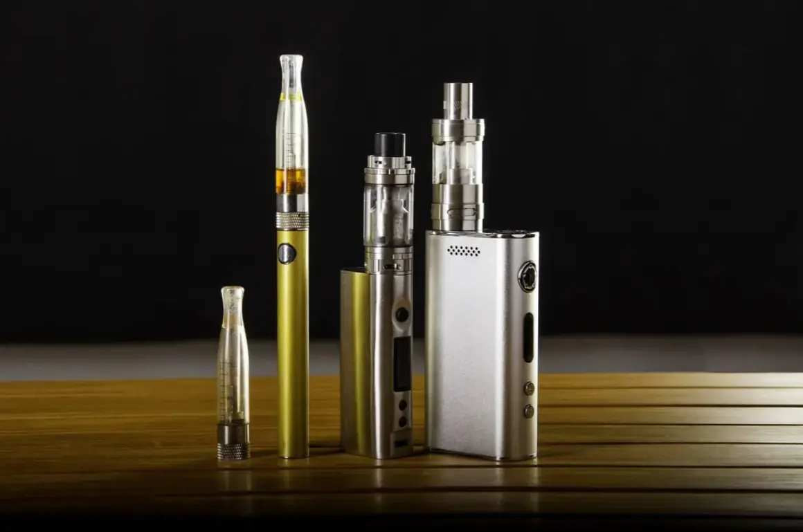 Collection de cigarettes électroniques, dont une dorée et une argentée, sur une table en bois. Ces appareils de vapotage, souvent à basse tension, offrent une alternative moderne.