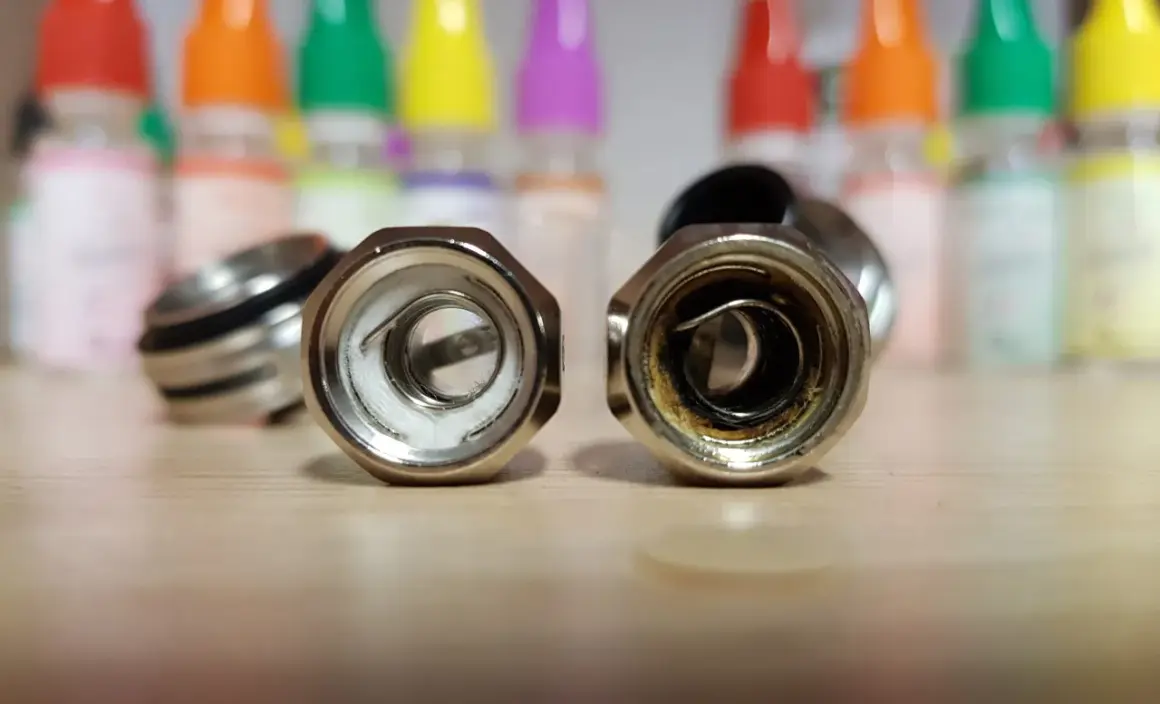 Deux résistances de cigarette électronique sur une table en bois. L'une est neuve, l'autre montre les signes d'une résistance crâmée après avoir vapoté.
