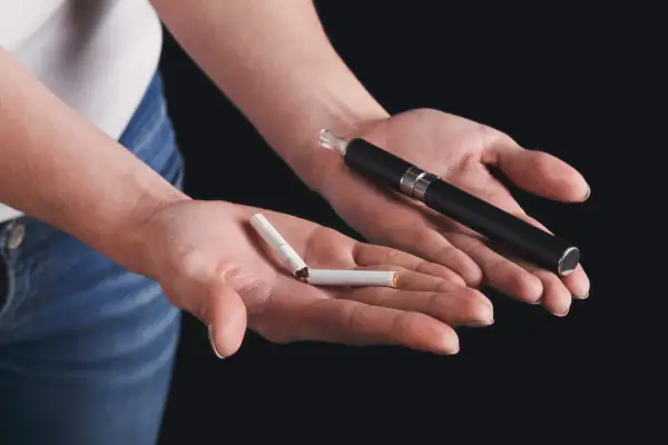 Deux mains présentent un choix : une cigarette électronique et une cigarette cassée. Un symbole pour arrêter de fumer.