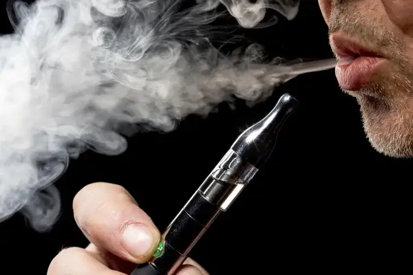 Un homme exhale une vapeur dense d'une cigarette électronique, un geste qui peut représenter un bienfait pour certains.