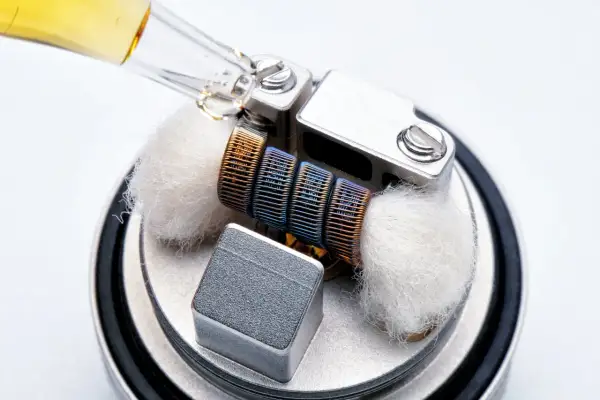 Goutte d'e-liquide sur un atomiseur prêt à l'emploi, avec ses mèches de coton et sa résistance colorée.