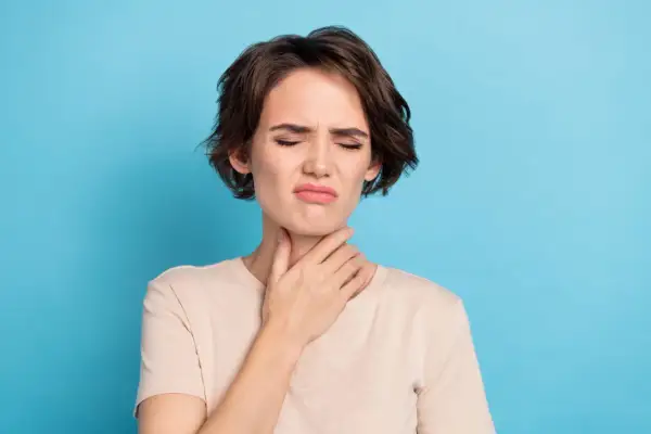 Femme avec la main sur la gorge, grimace, possible irritation due à une cigarette électronique gorge serrée.