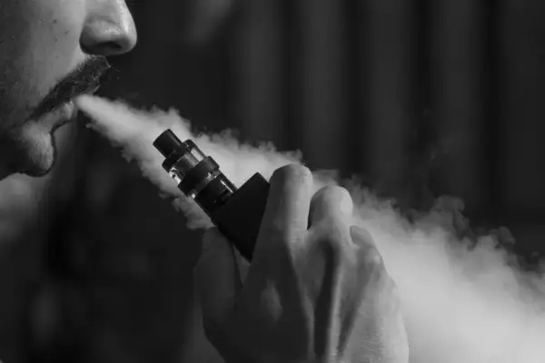 Un homme tire sur une cigarette électronique, exhalant un nuage de vapeur. Il ressent fatigue et vertiges.