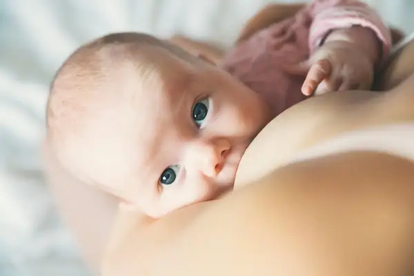Un bébé aux grands yeux bleus tète le sein de sa mère. L'allaitement est un moment précieux, loin des préoccupations comme la cigarette électronique.