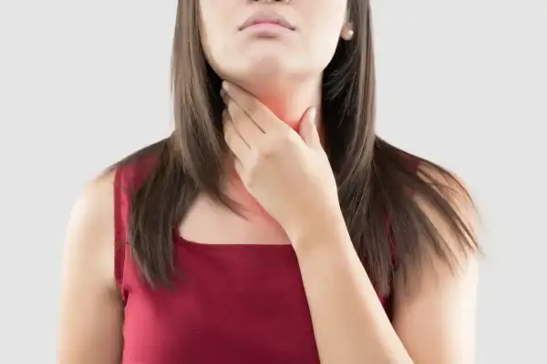 Une femme se tient la gorge, rouge et douloureuse, peut-être à cause d'une cigarette électronique.